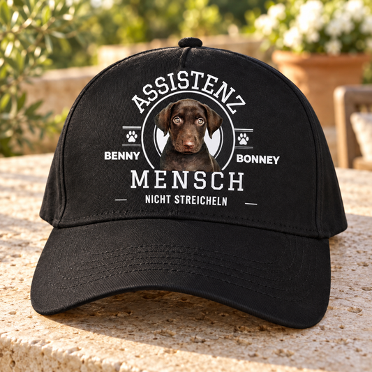 Gorra negra con estampado “ASSISTENZ MENSCH”, imagen de perro y el texto “NICHT STREICHELN”.