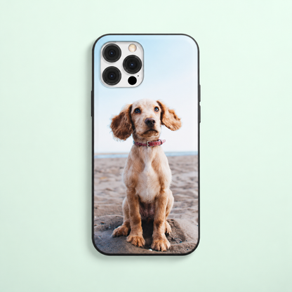 Funda de móvil con foto de un perro sentado en la playa, borde negro.