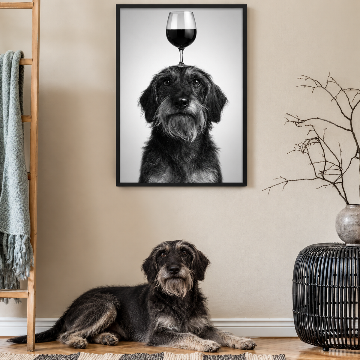 Póster en blanco y negro de un perro con una copa de vino en la cabeza, colgado en la pared. Un perro tumbado delante.