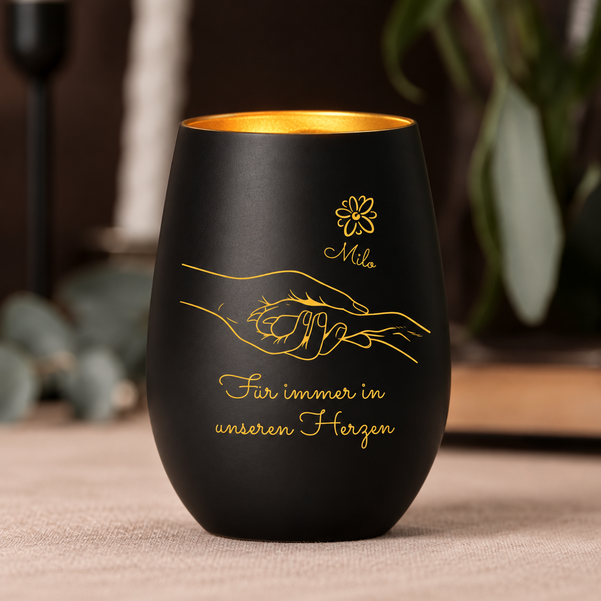 Luz conmemorativa negra con interior dorado, personalizada con diseño de manos y el texto "Für immer in unseren Herzen".