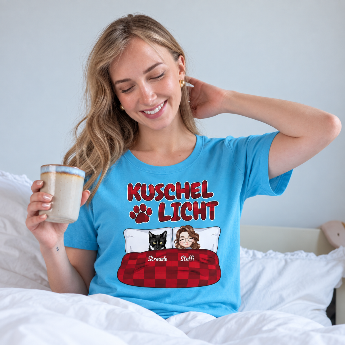 Camiseta turquesa con el texto "Kuschel Licht", en una mujer sonriente en la cama.
