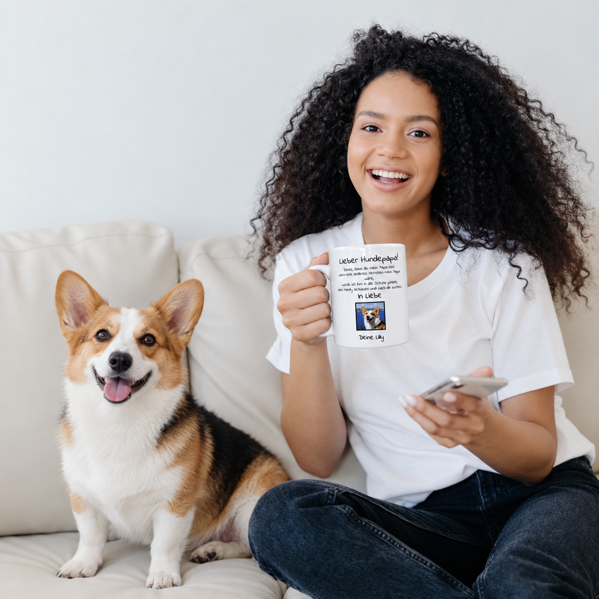 Persona con taza personalizada con el texto "Lieber Hundepapa" y foto, sentada en un sofá junto a un perro.