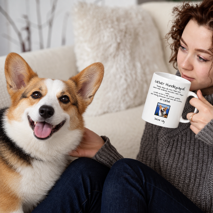 Persona bebiendo de una taza blanca con el texto "Lieber Hundepapa", un perro sentado a su lado.