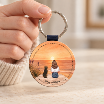 Llavero redondo personalizado con ilustración de una persona y un perro junto al mar al atardecer.
