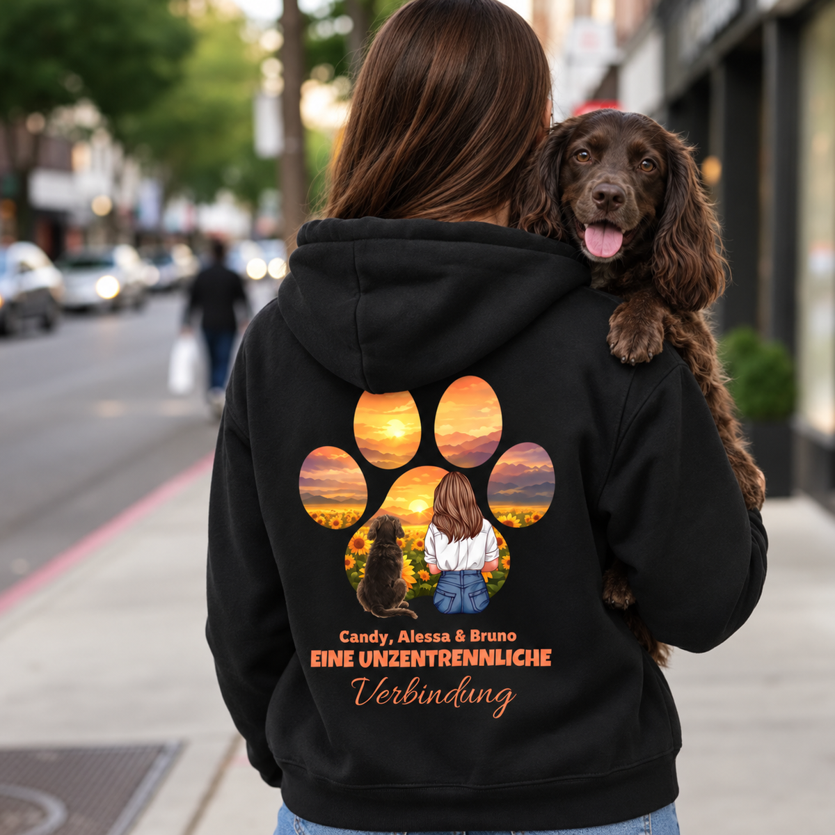 Sudadera con capucha negra con colorido motivo de persona y perro y el texto "Eine unzertrennliche Verbindung" en la espalda.