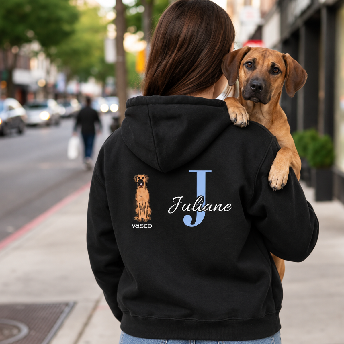 Sudadera con capucha negra con inicial personalizada "J" y motivo de perro en la espalda. La lleva una persona con un perro.