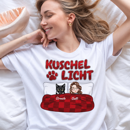 Camiseta blanca con el texto "Kuschel Licht" y un dibujo de una mujer y un gato en la cama.