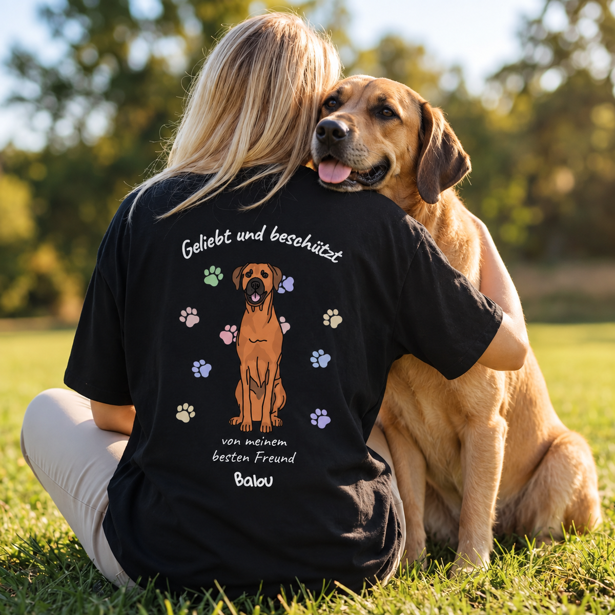 Camiseta negra con el texto "Geliebt und beschützt", un perro y huellas de colores.