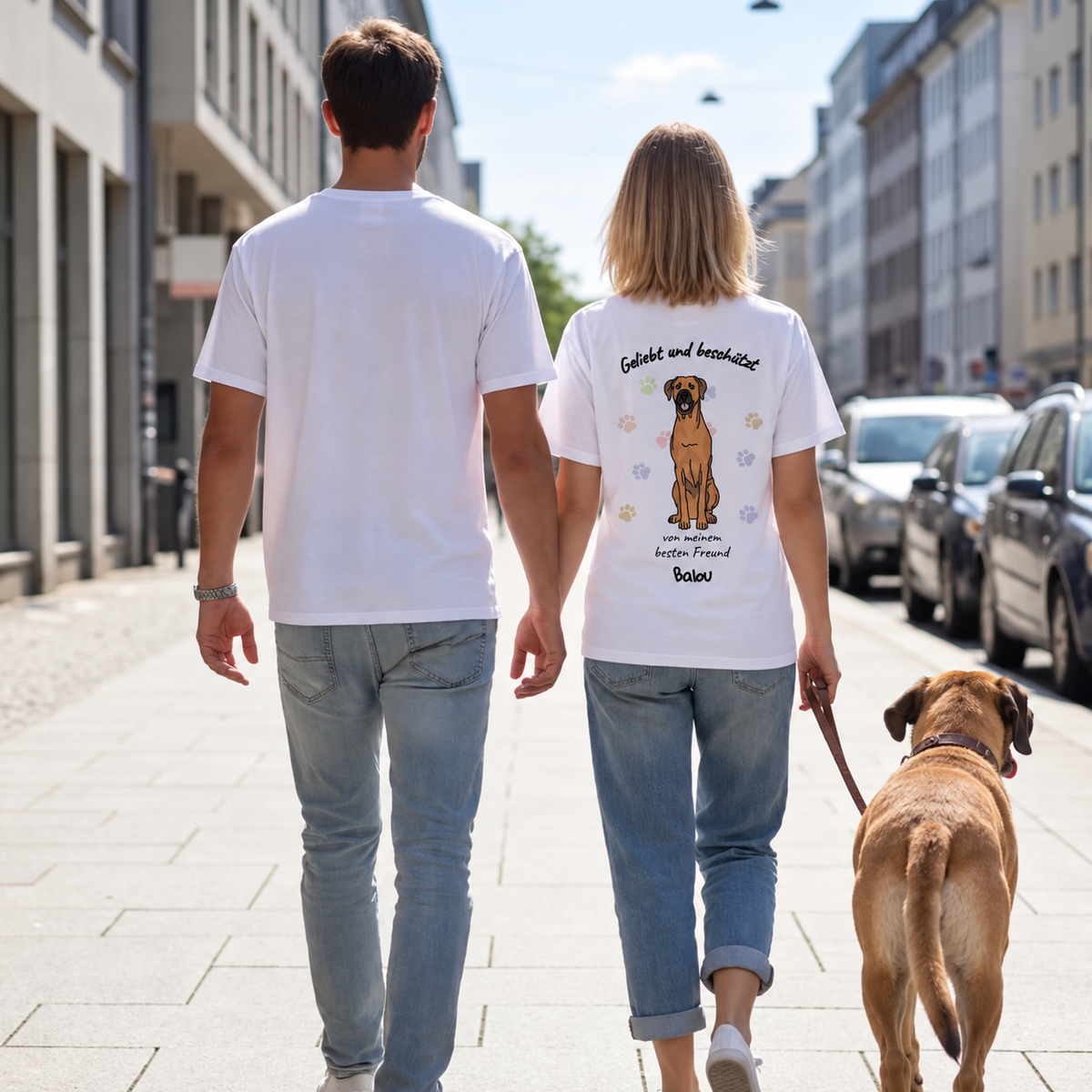 Dos personas con camisetas blancas con motivo de perro en la espalda, paseando un perro.