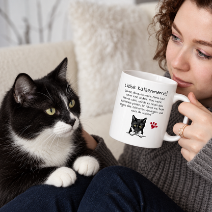 Taza personalizada con el texto "Liebe Katzenmama!" y motivo de gato, en manos de una mujer con un gato.