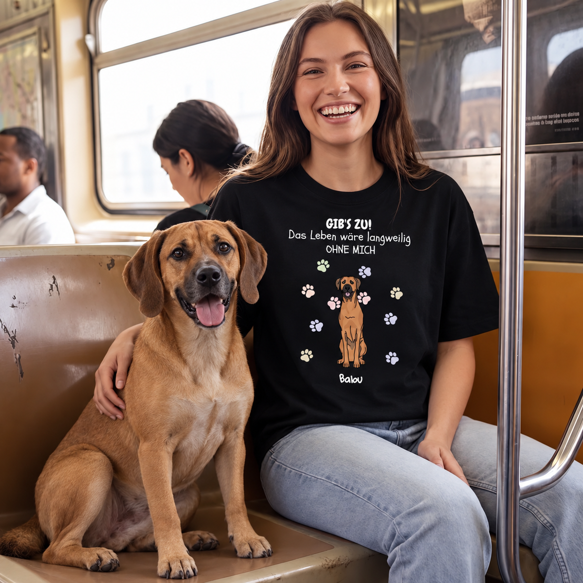 Camiseta negra con estampado, texto y foto de perro, llevada por una mujer sonriente en un tren. Perro sentado a su lado.