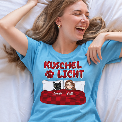 Camiseta azul con el texto "Kuschel Licht" y elementos gráficos de dos personas y un animal negro.