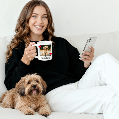 Mujer con jersey negro con taza personalizada con foto y perro, sentada en un sofá.