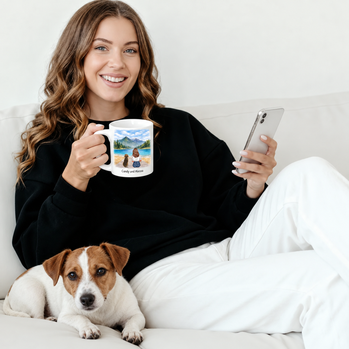 Persona sosteniendo una taza personalizada con paisaje, un perro tumbado a su lado en el sofá.