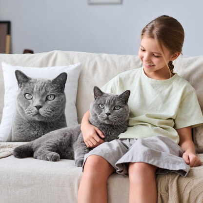 Cojín con estampado de gato gris en un sofá claro, una niña sentada junto a un gato gris.