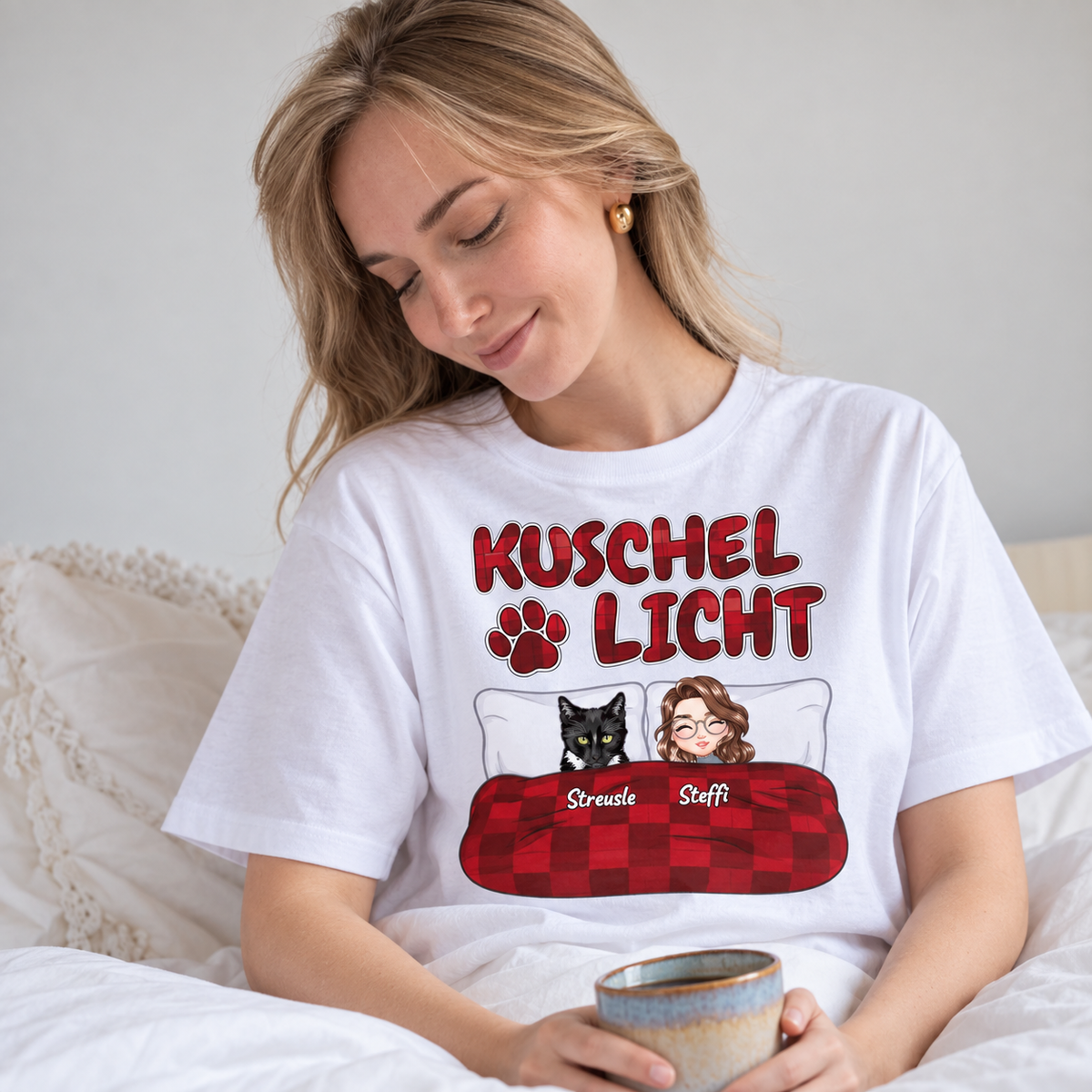 Camiseta blanca con el texto "Kuschel Licht" e ilustraciones de una mujer y un gato en la cama.