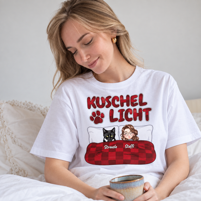 Camiseta blanca con el texto "Kuschel Licht" e ilustraciones de una mujer y un gato en la cama.