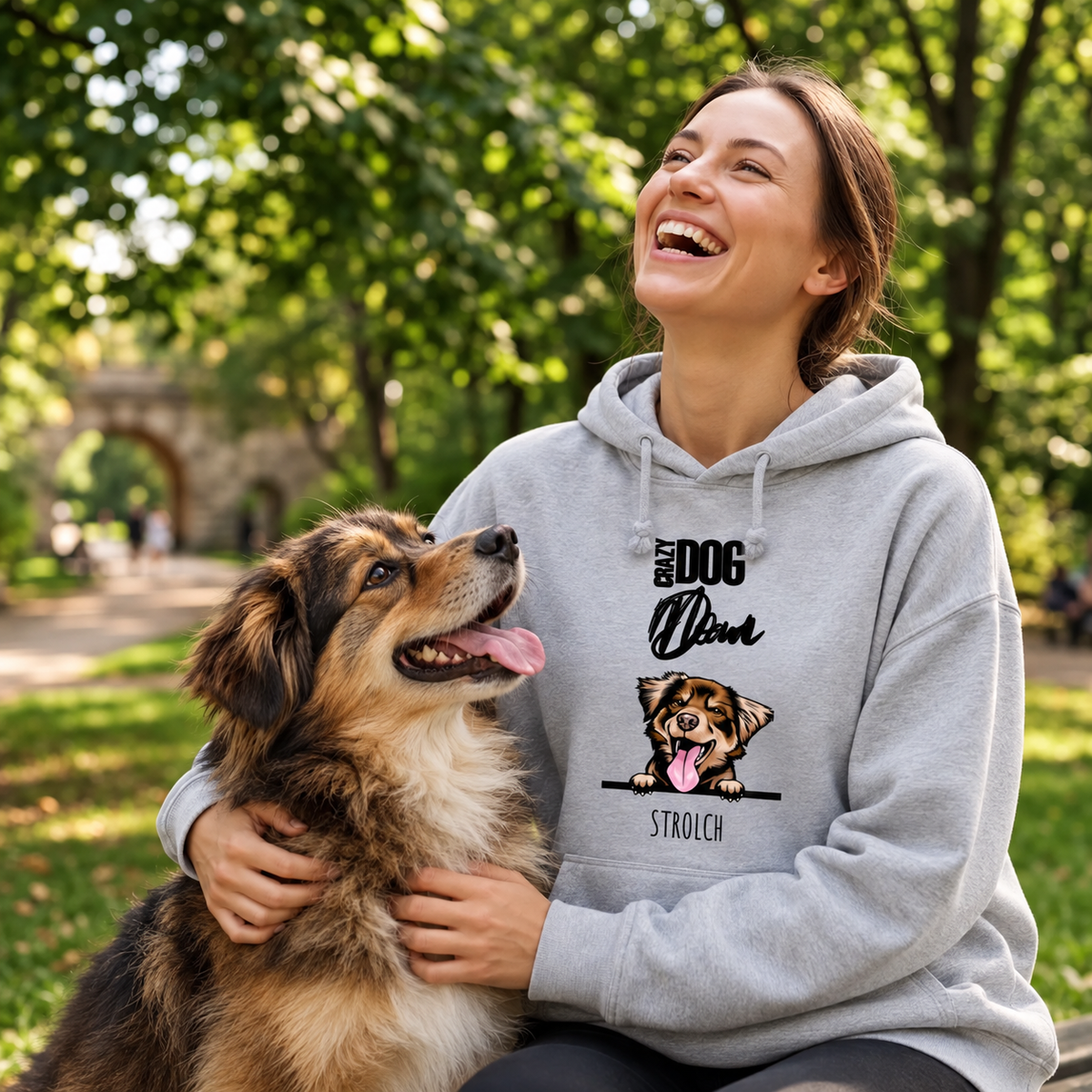 Sudadera con capucha gris con motivo de perro, llevada por una mujer que ríe y juega con su perro en el parque.