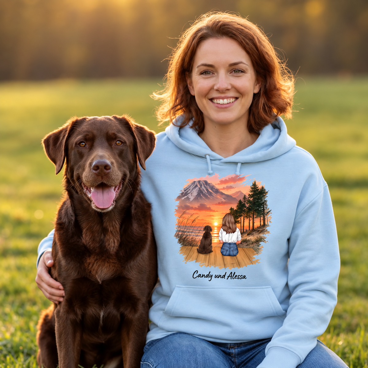 Chaqueta con capucha azul claro con gráfico de persona y perro ante un paisaje al atardecer.