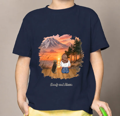 Camiseta infantil azul con gráfico de una persona sentada y un perro en un paisaje al atardecer.
