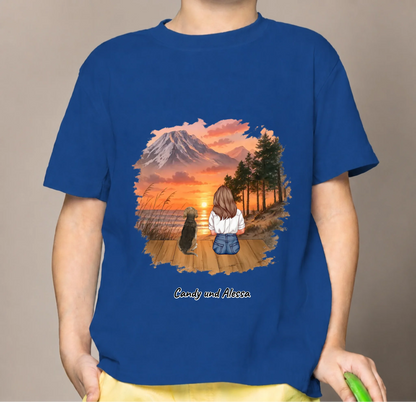 Camiseta infantil azul con ilustración de una niña y un perro contemplando el atardecer.