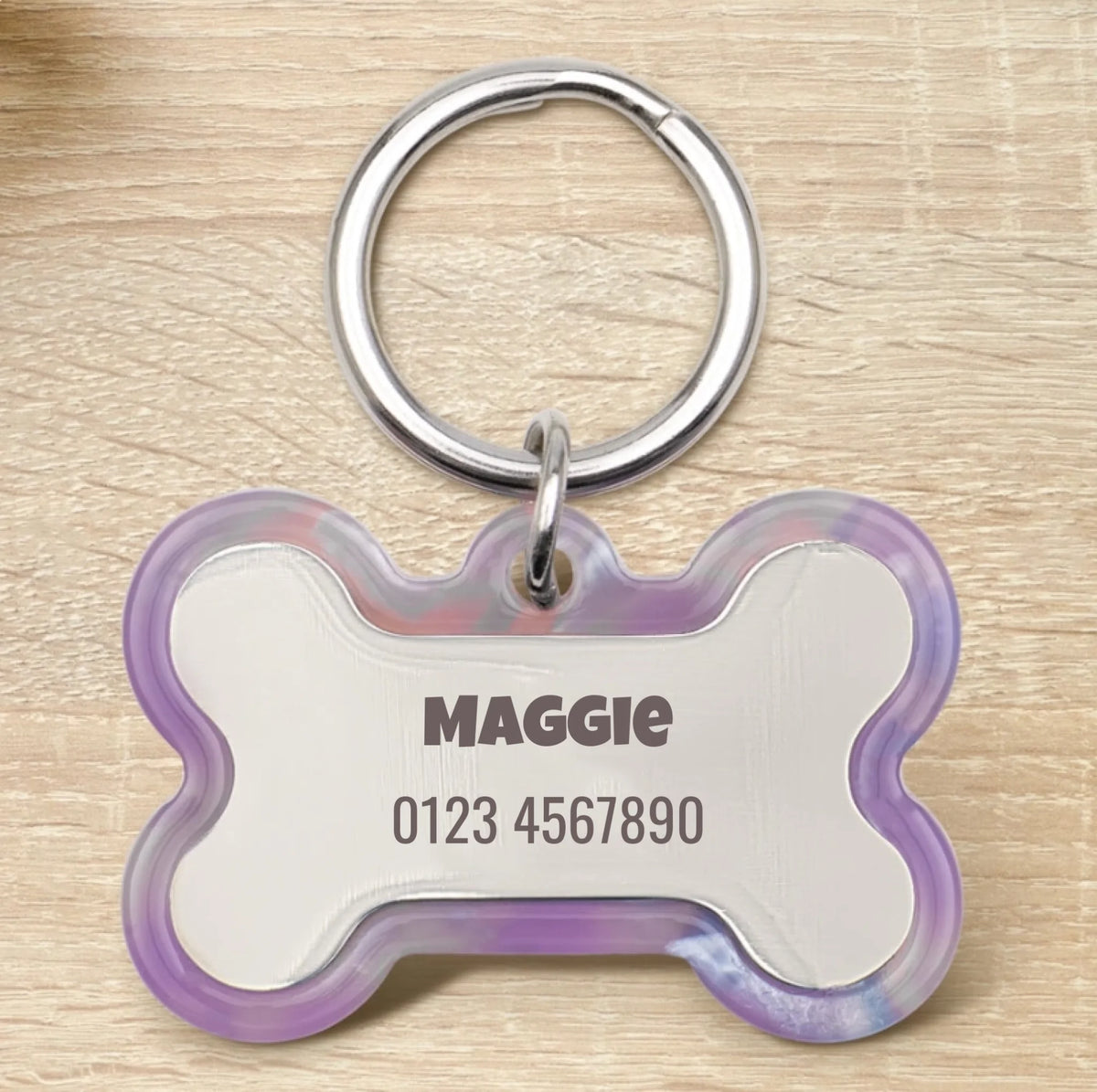 Placa para perro personalizada de resina epoxi en forma de hueso con anilla plateada y borde lila transparente.