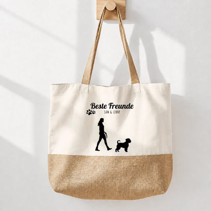 Bolsa de compras beige de tela con base de yute y estampado negro “Mejores amigos”. Silueta de una persona con un perro.