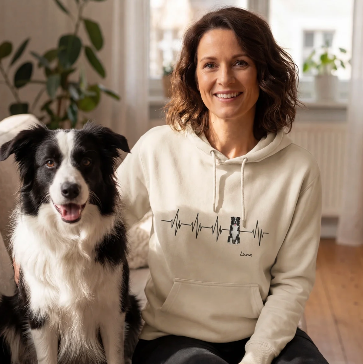 Sudadera con capucha beige con motivo de latido y texto personalizado, llevada por una mujer junto a un perro.