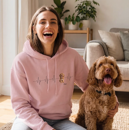 Persona con sudadera rosa con motivo de latido, sentada en una alfombra junto a un perro.