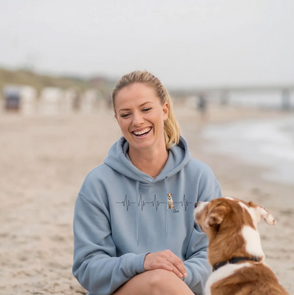 Sudadera con capucha azul personalizada con motivo de latido y perro, mujer sonriente sentada en la playa.