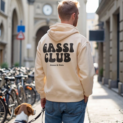 Persona con sudadera beige con "Gassi Club" en la espalda, de pie con un perro en una calle de la ciudad.