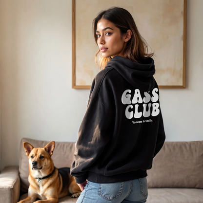 Sudadera con capucha negra con el texto "GASS CLUB" en la espalda, persona con un perro en un salón moderno.