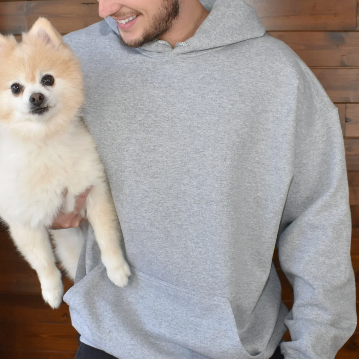 Sudadera gris con capucha grande, llevada por una persona que carga un pomerania.
