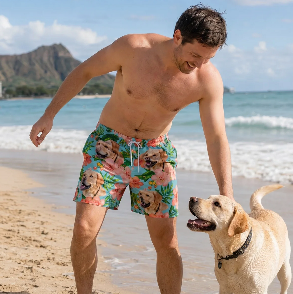 Hombre en la playa con bañador colorido con perros y flores. Un labrador juega en la arena a su lado.