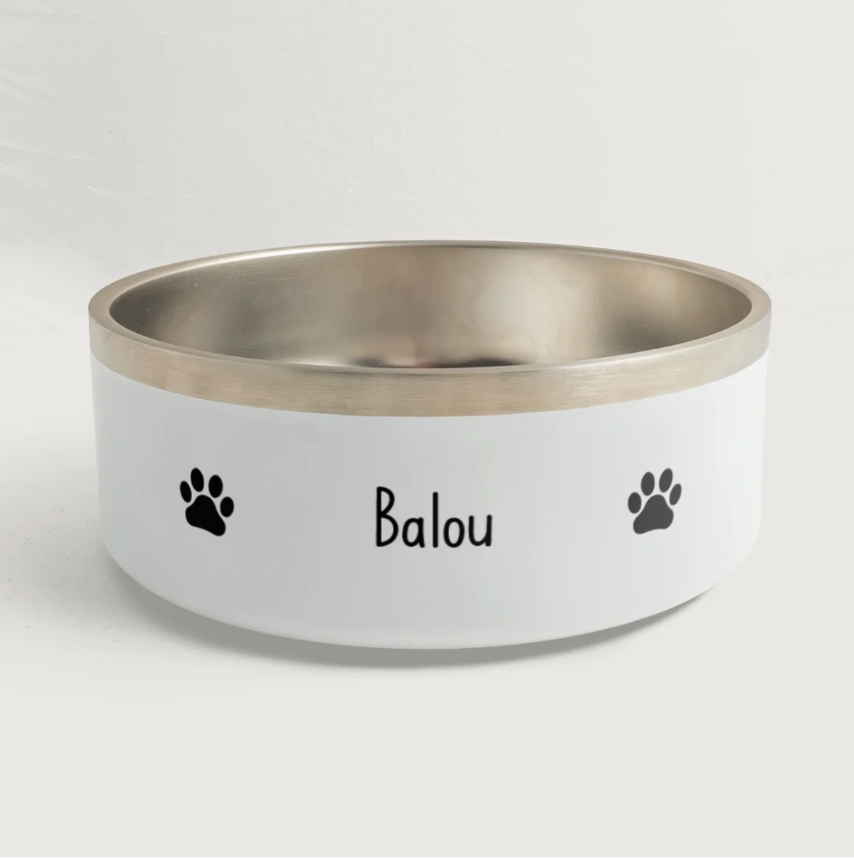 Comedero personalizado con borde plateado, el nombre "Balou" y huellas de patas negras.
